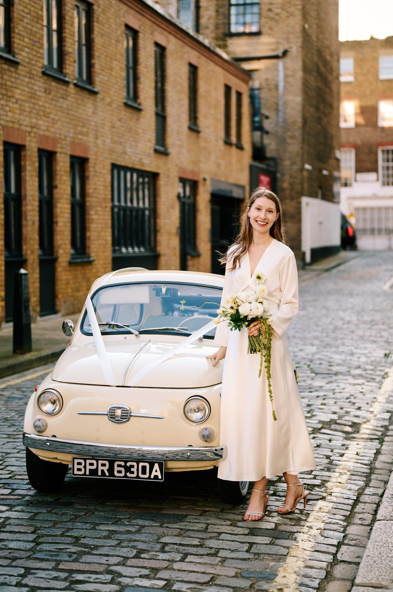 Bride standing beside a vintage car ahead of her small London wedding