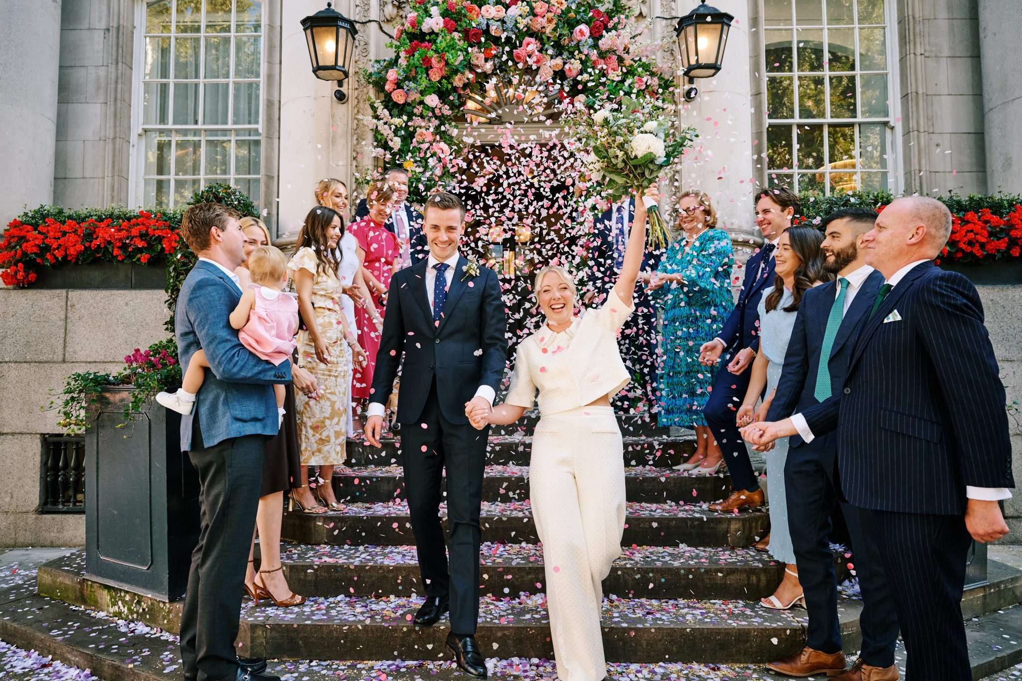 Newlyweds surrounded by confetti and guests on the steps of their venue